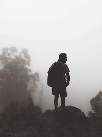 Rear view of silhouette young man with backpack standing on mountain during foggy weather