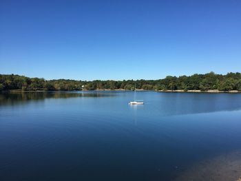 Boat sailing in lake against clear blue sky