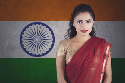 Portrait of smiling woman wearing maroon sari standing against indian flag