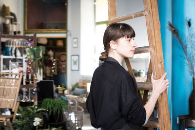 Side view of young female entrepreneur carrying ladder at store