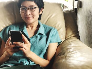 Portrait of smiling young man using mobile phone while sitting on sofa