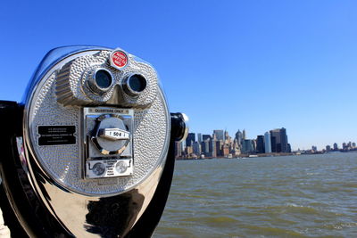 Close-up of coin-operated binoculars by river against clear blue sky at ellis island