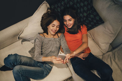 High angle view of smiling friends using phone while resting on sofa at home