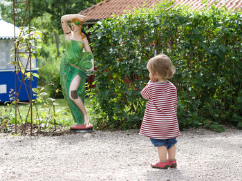 Rear view of girl standing against statue and plants in park