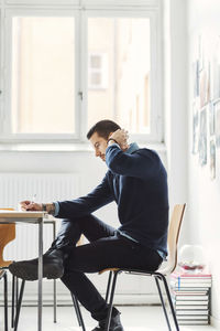 Side view of mid adult businessman writing in book at office desk