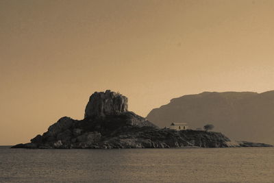 Rock formation in sea against clear sky during sunset