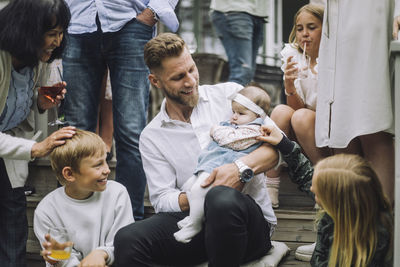Family playing with toddler girl held by man sitting on steps