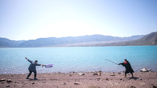 Men fishing in lake against clear sky