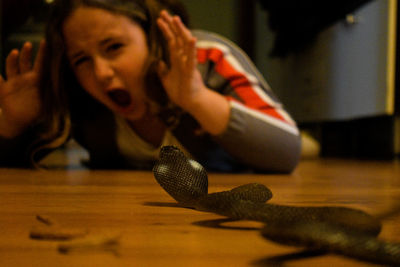 Close-up of scared girl with artificial snake at home