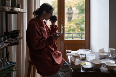 Side view of young woman using mobile phone while standing at home