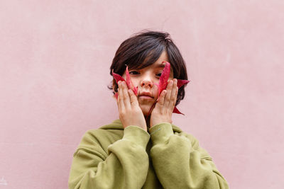 Smiling girl holding big red leaves at her face