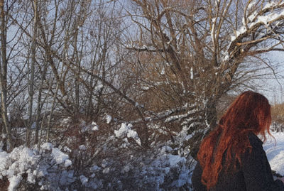 Woman standing by bare trees during winter