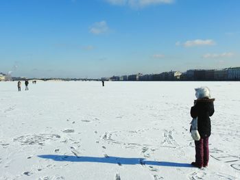 Boy standing on snow covered beach against sky