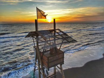 Lifeguard hut on beach against sky during sunset