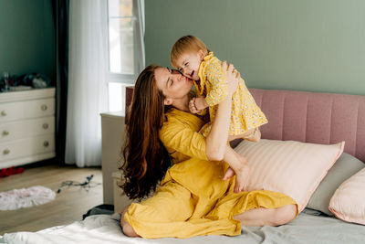 Side view of mother and daughter sitting on bed at home