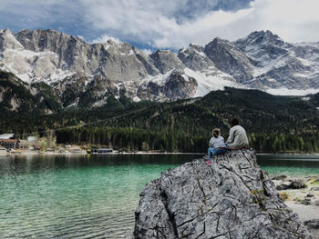 People on rock by mountains against sky