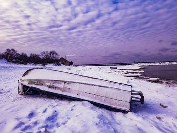 Abandoned boat on snow covered shore against sky