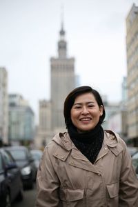Portrait of cheerful woman standing amidst buildings in city