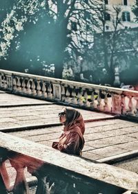 Side view of man sitting on railing against bridge