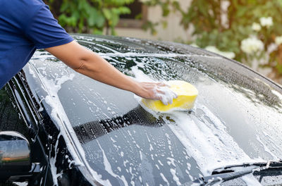 Hand hold yellow sponge with foam soap on outdoor holiday.