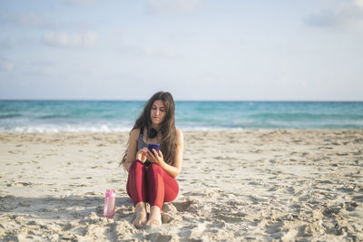 Young woman standing at beach against sky