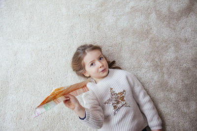 Portrait of girl holding paper airplane while lying on rug