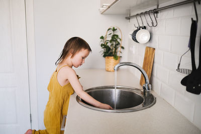 European child of 4 years with water for drink with glass in sink on bright kitchen in real interior