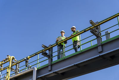 Engineers standing on bridge at recycling center under blue sky