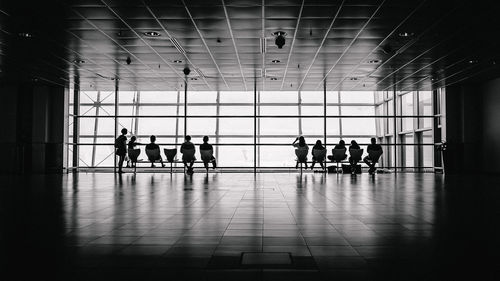 Silhouette people walking in airport seen through glass window