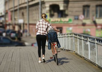 Rear view of woman with bicycle on wooden bridge during sunny day