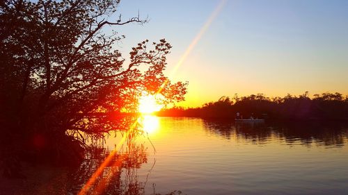 Silhouette trees by lake against sky during sunset
