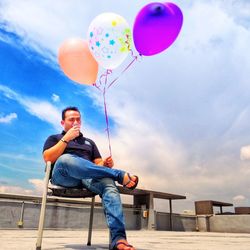 Low angle view of man holding balloons against sky