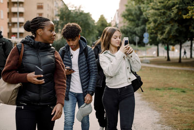 Teenage girls and boy using mobile phone while walking on street in city