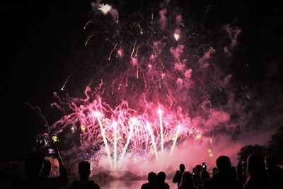 Silhouette people looking at firework display during night