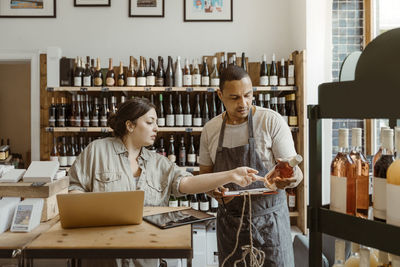 Male and female owners discussing holding wine bottle at shop