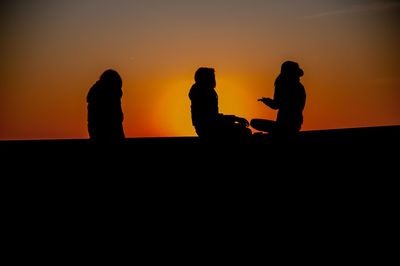 Silhouette people against orange sky during sunset