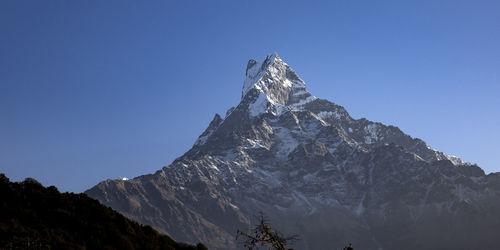 Low angle view of snowcapped mountains against clear blue sky