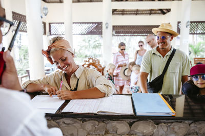 Happy woman signing at reception desk during check in with family at resort