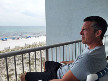 Generation x business man on vacation sitting on deck of beach condo relaxing .