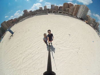 Fish-eye view of friends standing on sand against cityscape