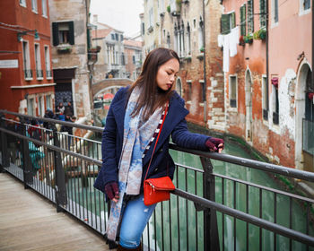 Young woman standing on footbridge over canal in city