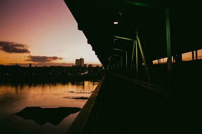 Illuminated city by river against sky at sunset