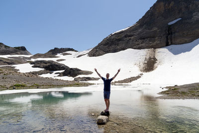 Man standing on rock in lake against mountains during winter