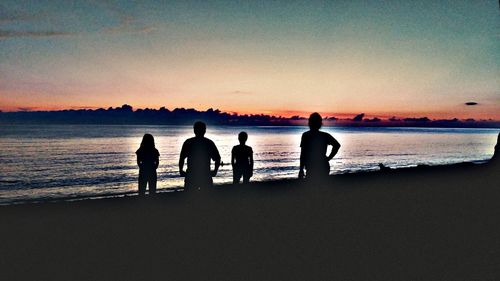 Silhouette people standing on beach against sky during sunset