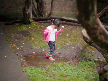 Full length of girl holding camera standing in puddle standing at park