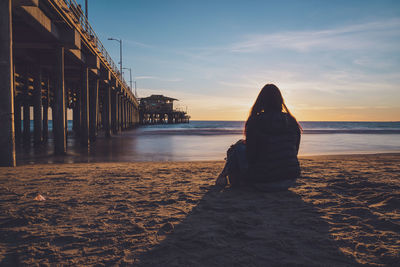 Rear view of woman sitting on beach during sunset