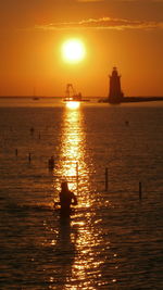 Rear view of person standing in sea during sunset