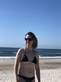 Young woman wearing sunglasses on beach against clear sky