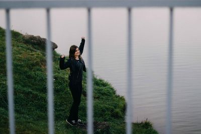 Full length of young woman standing by lake seen through railing