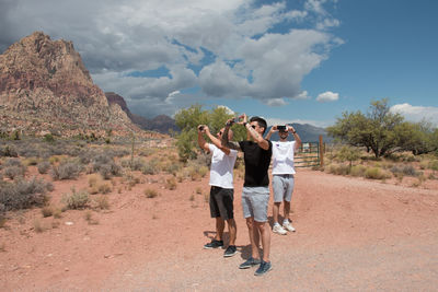 Full length of friends standing on rock against sky